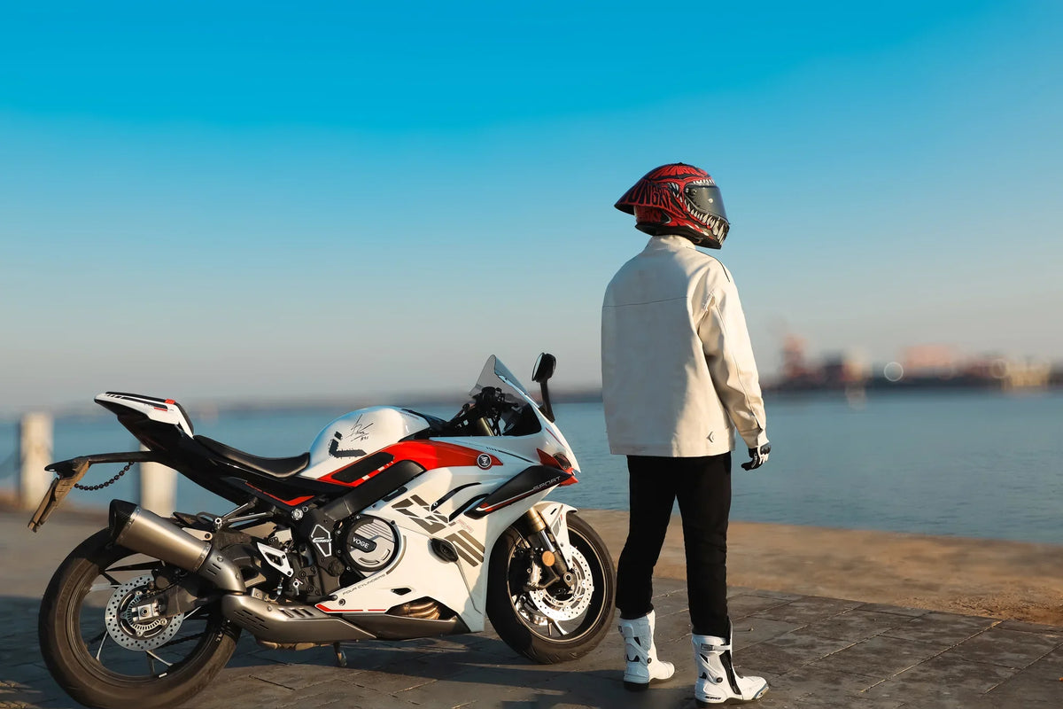 Rider in a red helmet standing beside a sport bike by the sea