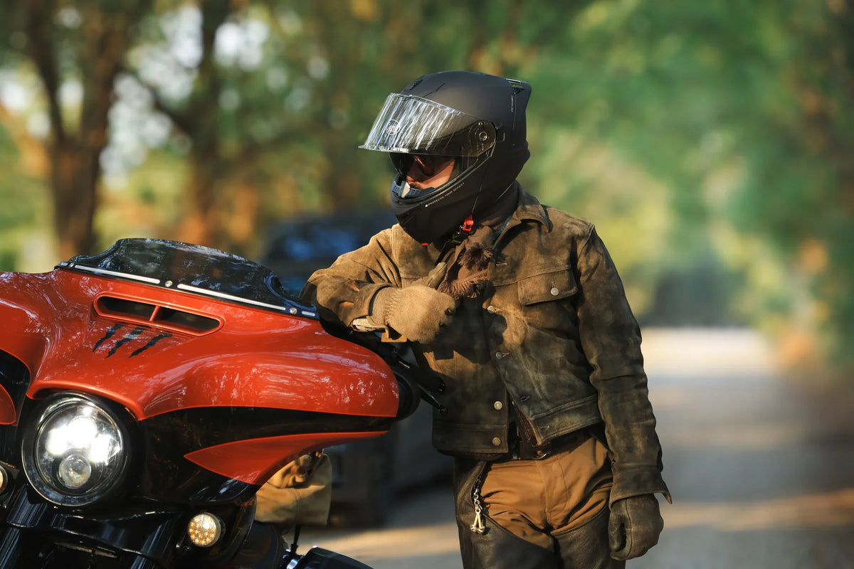 Rider in a full-face helmet and canvas jacket leaning on an orange touring bike