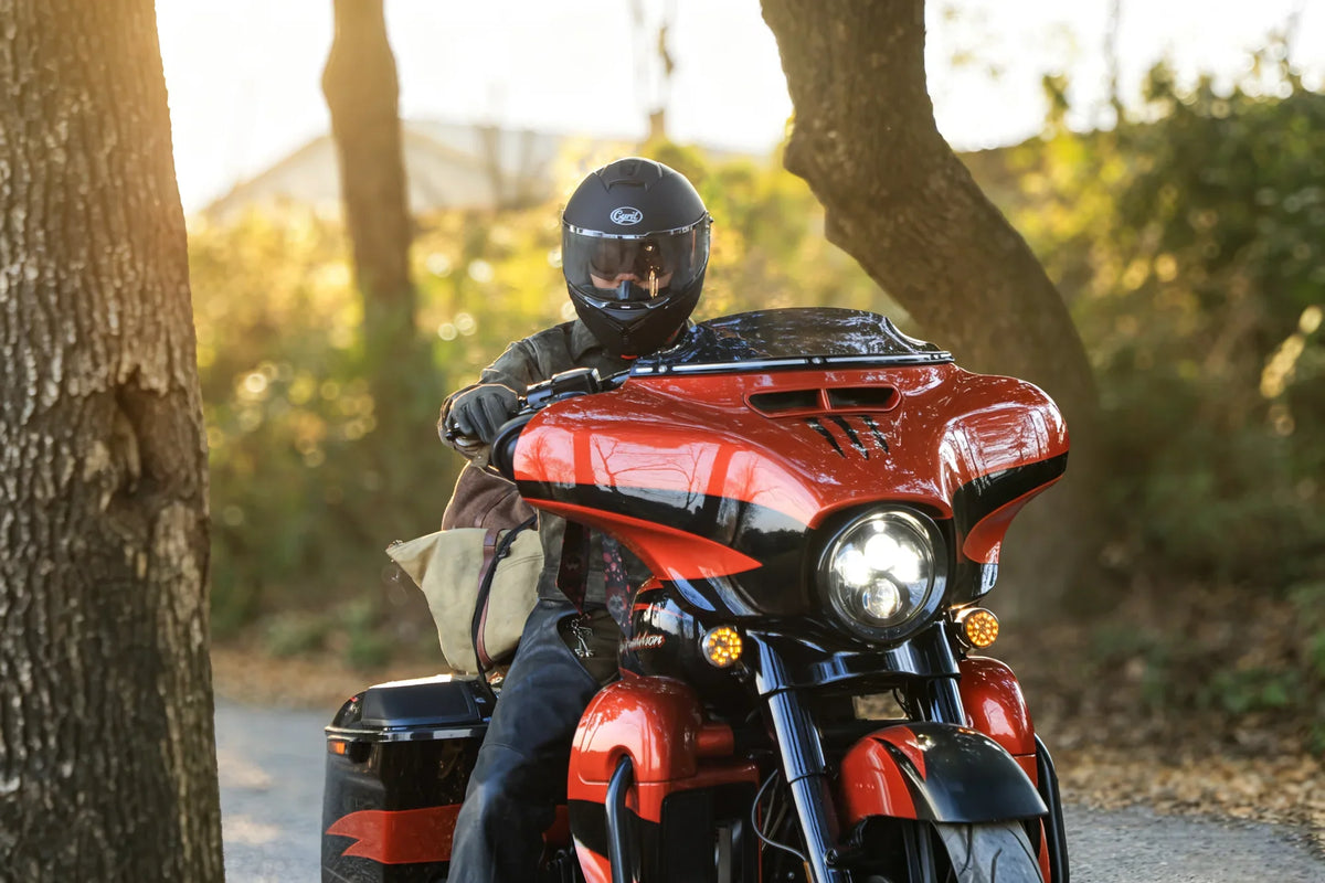 Rider in a full-face helmet on a red touring motorcycle in the woods