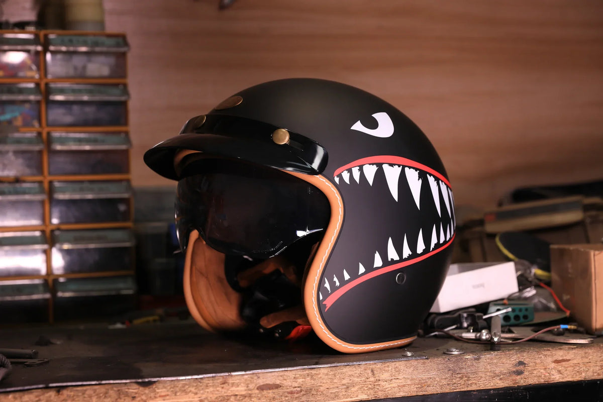 Matte black open-face helmet with a shark-teeth graphic on a workshop shelf