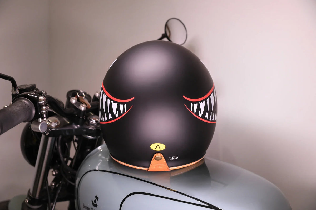 Matte black open-face helmet with a shark-teeth graphic on a vintage motorcycle