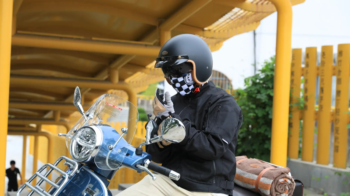 Rider in a black open-face helmet with a checkered visor on a vintage scooter